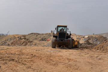 Bulldozer working on a construction site, clearing sand and debris under a cloudy sky.
