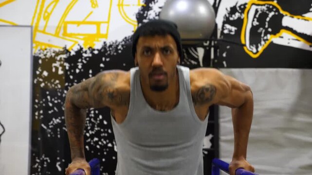 Strong african athlete doing push ups on parallel bars at sport club. Muscular afro american sportsman with tattoos doing hard exercises modern gym. Concept of healthy and active lifestyle. Slow mo