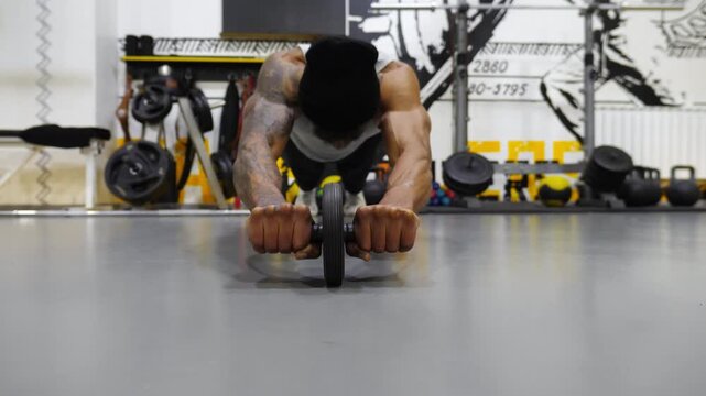 Muscular african sportsman doing exercises with ab roller at fitness centre. Young afro american athlete hard training with gymnastic wheel at modern gym. Strong black man working out at sport club