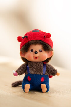 A Monchhichi doll keychain wearing a red hat sits on a wooden surface, capturing nostalgic toy culture and collectible character design in soft natural light.