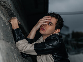 Young caucasian male in leather jacket posing against urban backdrop