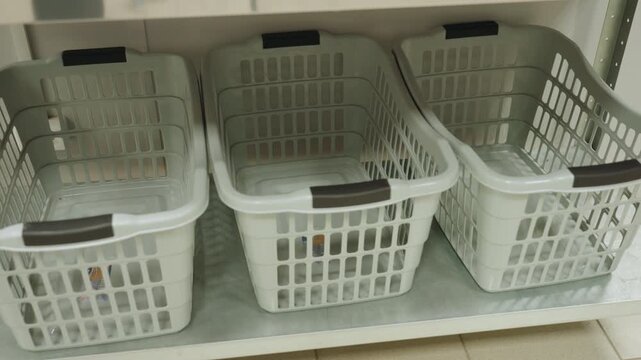 High angle view of white laundry baskets neatly arranged on metal shelf inside laundry facility, showcasing clean empty plastic containers used for organizing or carrying clothes in service