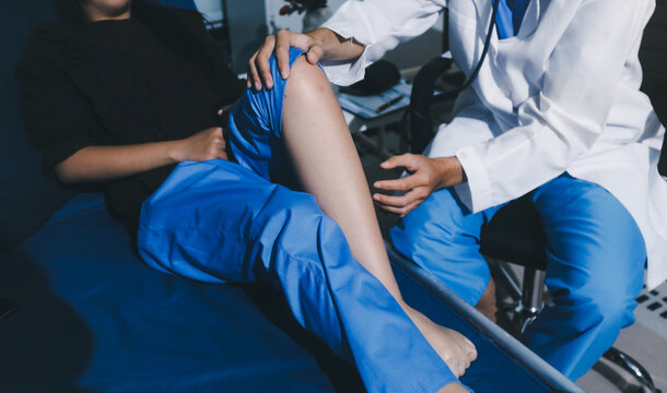 Asian male doctor examining foot of female patient sitting on bed in hospital room. Performing medical checkup. Diagnosing injury. Providing healthcare. Podiatry. Physical therapy. And rehabilitation