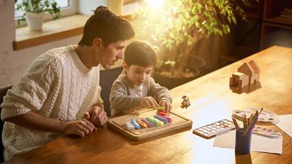 Father and son playing with modeling clay at wooden table. Concept of creative learning, fine motor...