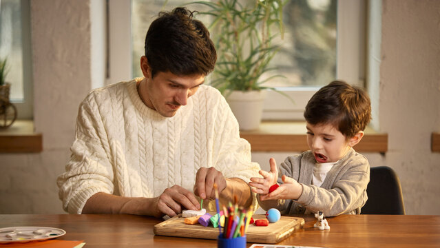 Father helping son shape clay during creative playtime. Concept of early education, parental guidance, fine motor skills, shared activities, and supportive family environment.