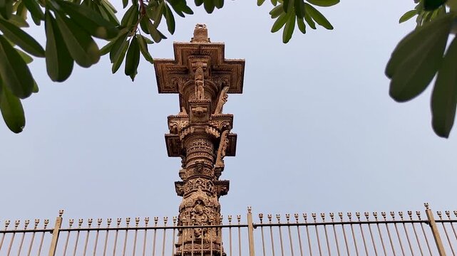 Vadnagar, Gujarat, India Kirti Toran stone pillar rising against sky, framed by green tree leaves, ancient Indian architecture, carved monument, cultural heritage landmark, and historic tourism site.