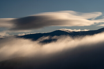 Fototapeta premium Cloud formations drift over mountain peaks during early morning hours in a rural area. Winter Hiking in Carpathian Mountains, Ukraine
