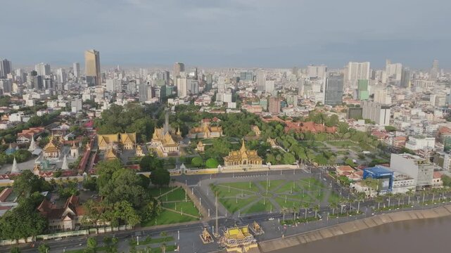 Aerial drone high angle view showing Royal Palace complex with green gardens, riverfront road, and surrounding city skyline under daylight in Phnom Penh