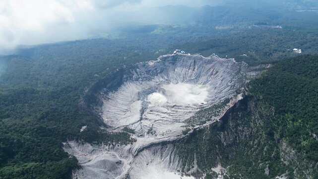 Cinematic drone shot of a large Tangkuban Perahu volcanic crater in Bandung, Indonesia surrounded by lush green mountains and emitting smoke.