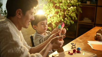 Father and son concentrating while building clay shapes together. Concept of mindful parenting,...
