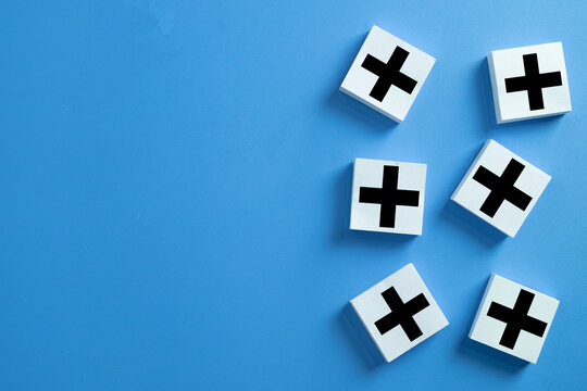 White wooden blocks with plus symbol on blue background. Concept of positive thinking, added value, benefits, and profit growth. Minimalist flat lay design with copy space.