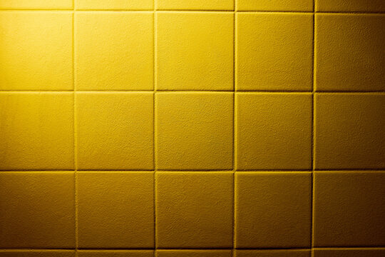 Yellow padded wall panels with square grid geometry, soft fabric texture and gentle depth. Structured background with warm tone, tactile surface and controlled studio lighting. Copy space