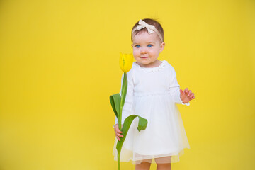Cheerful happy child with tulip flower. little girl in white dress on yellow background. 