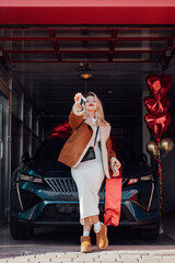 Joyful woman receiving a new car as a gift with decorative red ribbon and heart-shaped balloons