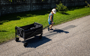 Child pulls a four-wheel folding wagon with toys and accessories during a tourist trip