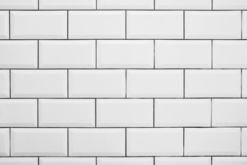 White subway tile wall with clean grid pattern and glossy ceramic finish. Modern architectural background featuring structured negative space and practical copy space for design use.