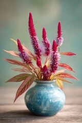 Fototapeta premium A blue ceramic vase holds tall, pink, feathery flowers with reddish leaves on a wooden table. Concept Blue ceramic vase, Pink feathery flowers, Reddish leaves, Wooden table, Still life decor