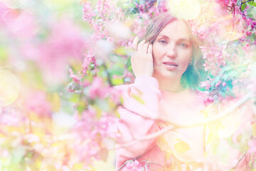Fototapeta premium Springtime background, a woman in pink in a blooming cherry orchard, a model posing in a romantic style