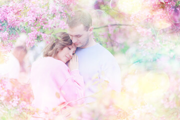 A couple in love among a pink cherry blossom in spring, a man and a woman hug