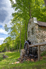A decorative stone structure features an old wooden water wheel set against a lush green forest background.