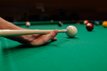 A person's hand using a cue stick to aim at a white cue ball on a green felt pool table.