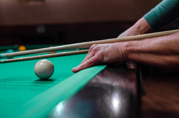 A person's hand using a cue stick to aim at a white cue ball on a green felt pool table.