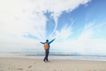 A guy with a backpack against the blue sky on the coast