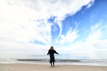 A woman in a coat dances by the sea, the concept of freedom and springtime relaxation