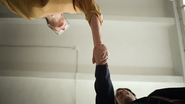 Bottom view pov shot of Caucasian business couple shaking hands for closing deal or successful meeting in office setting