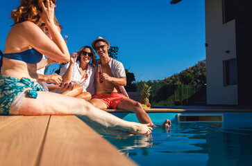 Group of middle aged friends enjoying fruit and drinks by swimming pool.