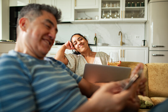 Happy couple relaxing with wine and devices at home
