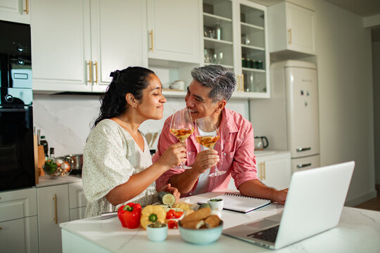 Smiling couple toasting wine while cooking together in a home kitchen