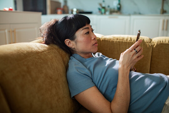 Woman relaxing on sofa using smartphone at home