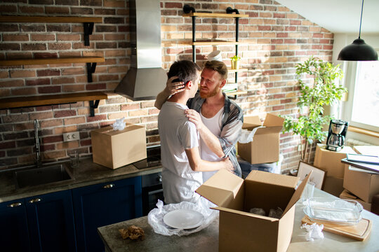 Two men embrace while unpacking in new home kitchen