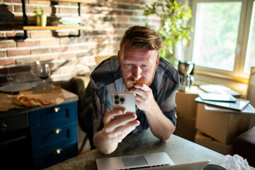 Thoughtful man using smartphone while working from home kitchen