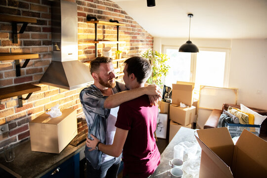 Happy gay couple hugging while unpacking in new apartment kitchen