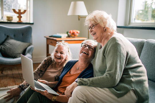Three senior women laughing with laptop at home