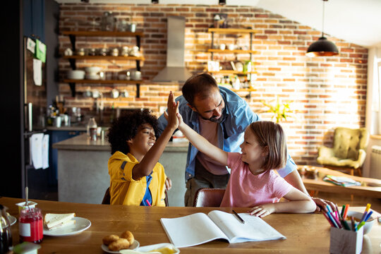 Dad supporting children with homework in home kitchen