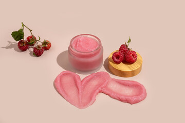 jar of natural body scrub, a swatch of scrub and raspberry berries on a beige background