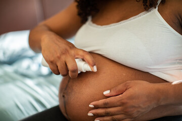 Pregnant woman applying belly lotion at home