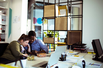 Coworkers sharing smartphone during lunch break in modern office