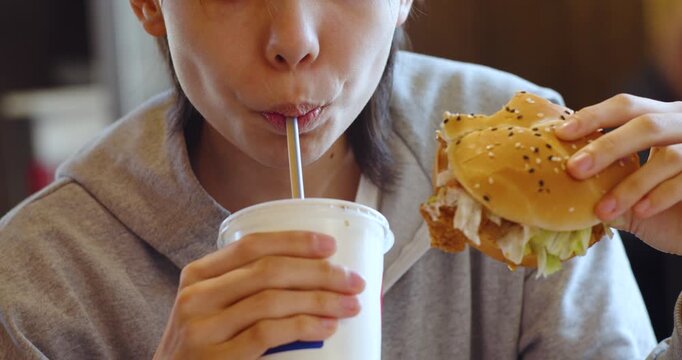 Slow motion video of a teenage girl sits comfortably in a fast food cafe, sipping soda and enjoying a relaxed moment surrounded by the vibrant, casual atmosphere.