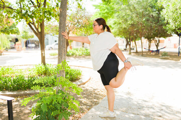 Active plus size woman doing a quad stretch outdoors in a park, preparing for exercise and focusing on fitness and wellbeing © AntonioDiaz