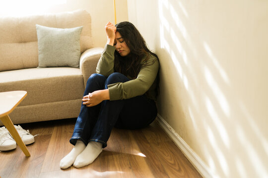 Young woman feeling sad and alone, experiencing depression or anxiety while sitting on floor at home