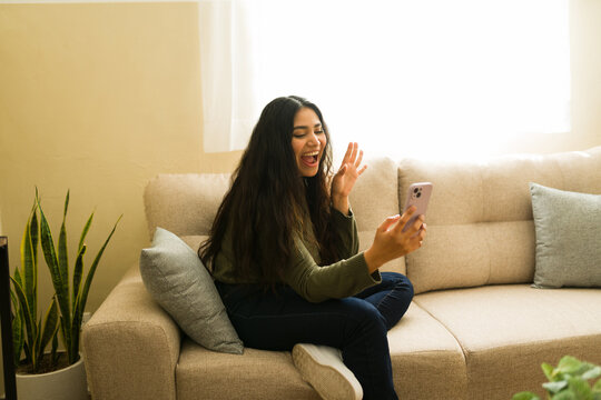 Hispanic woman smiling and waving during video call on smartphone, communicating with friends or family at home - Powered by Adobe