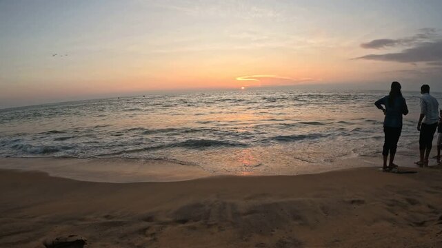 Sunset at beach over Arabian Sea, three people watching sunset