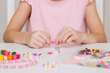 Girl hands making colorful bracelet on white table at home room. Creating different beaded jewellery. Little child handcraft. Closeup. Front view.