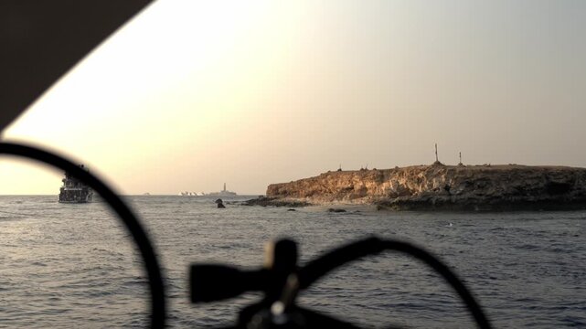 Little Brother Island during sunset. The rocky, arid cliffs of the island are illuminated by the warm, fading light, casting golden tones over the stone and the dark, choppy waters of the Red Sea.