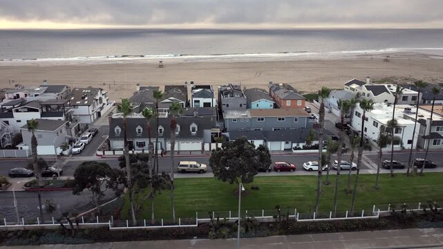 High-angle aerial shot of luxury beachfront homes in Newport Beach, California under cloudy skies. Rainy weather softens the coastal landscape, reflects a slower pace along the Orange County shoreline