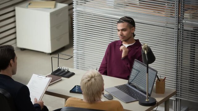 Zoom in slowmo shot of young Black male job seeker answering questions during interview with HR managers in modern office space